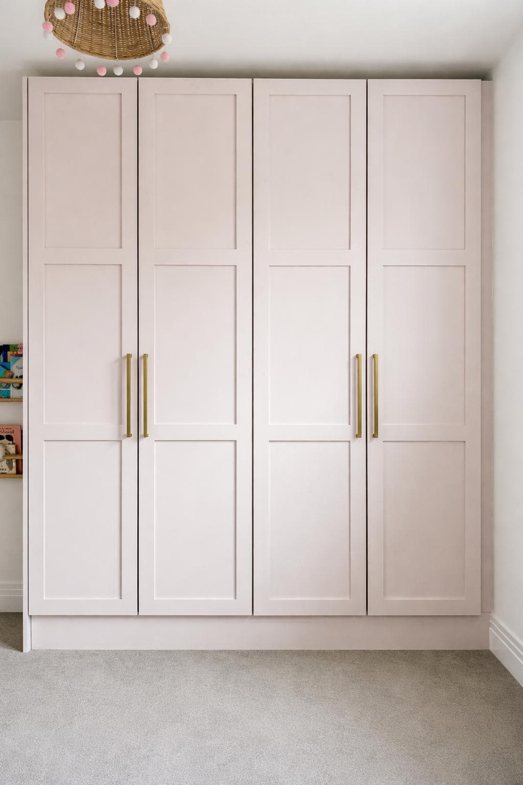 Pink hand-painted fitted wardrobes with brass handles in a child's bedroom