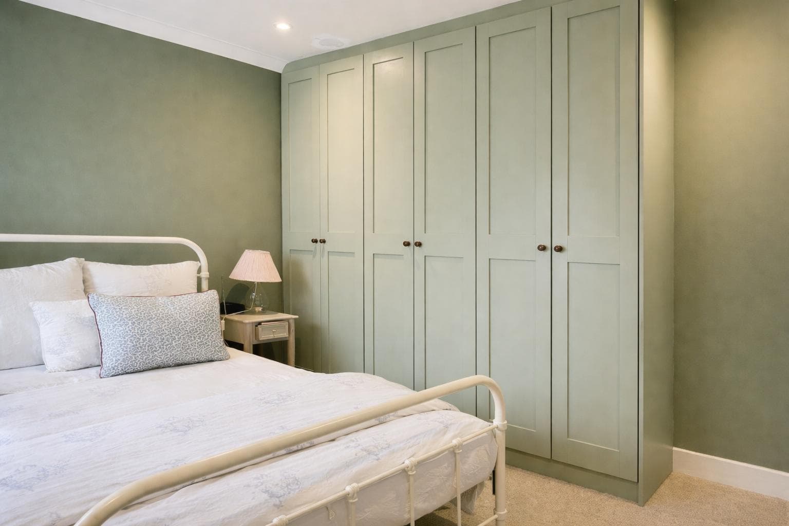 Sage green fitted wardrobes built floor to ceiling across a bedroom wall